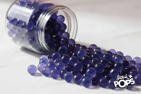Tarro de vidrio volcado con popping boba de arándano morado esparcido sobre una mesa blanca